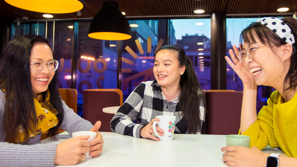 Three people are sitting at a table with coffee cups and laughing together.