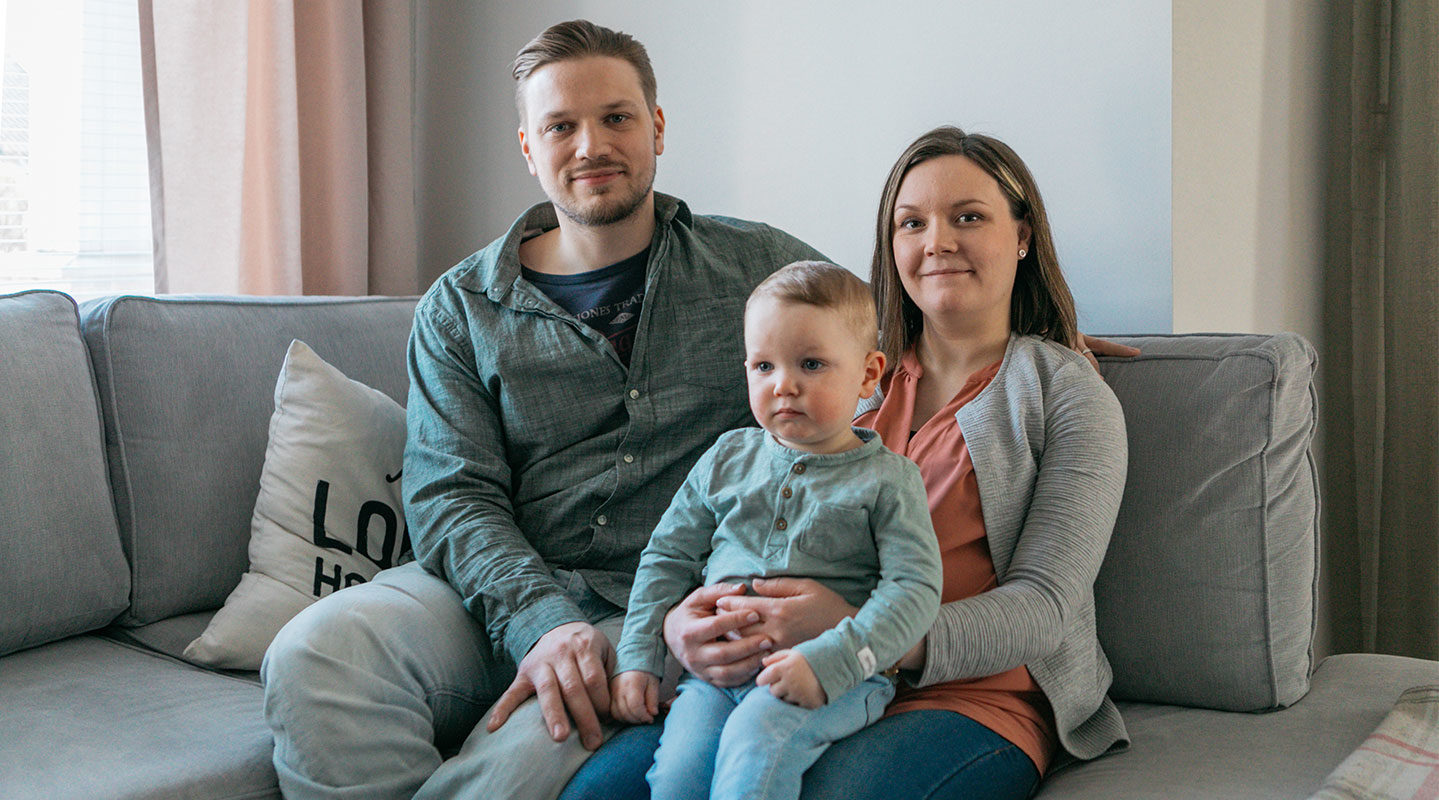 Markku, Emilia ja heidän pieni lapsensa istumassa sohvalla.