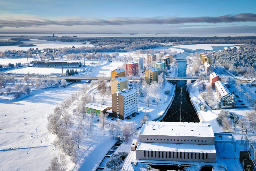 Aerial photo of the Oulu River estuary in the winter. Along the river, there are tall, colourful apartment buildings. In the photo there is a street with bridges. The Merikoski power station can be seen in the foreground.