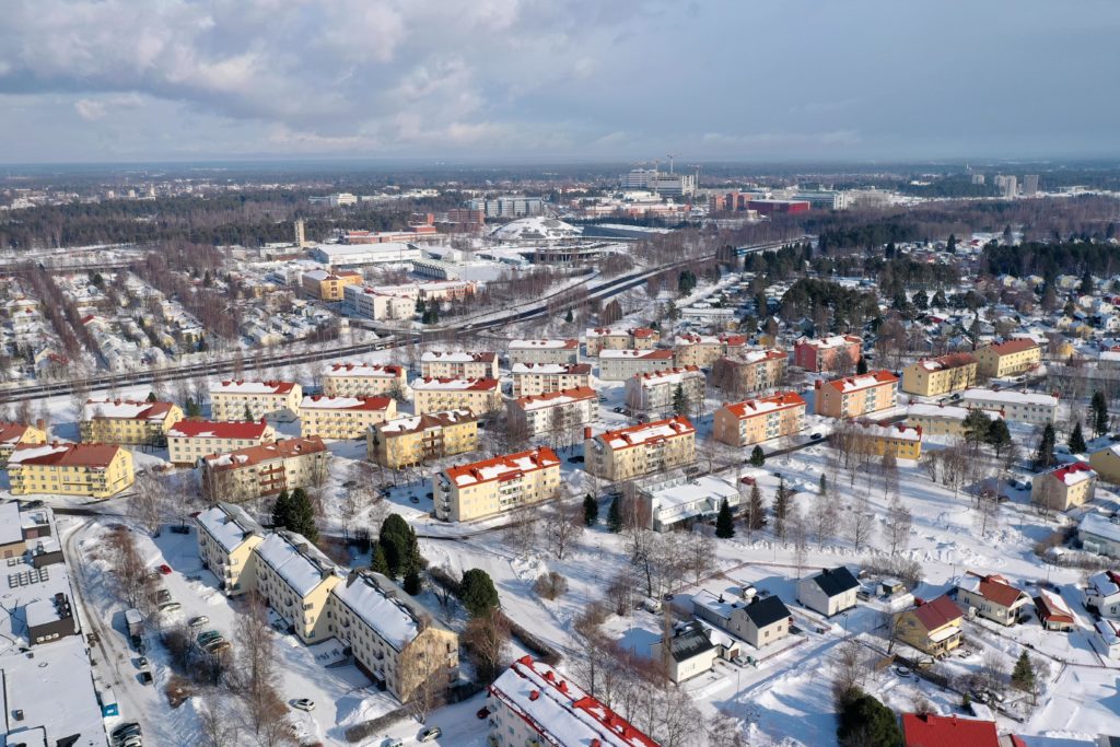 Aerial photo of wintry Oulu. Several yellow apartment buildings with red roofs can be seen in the photo.