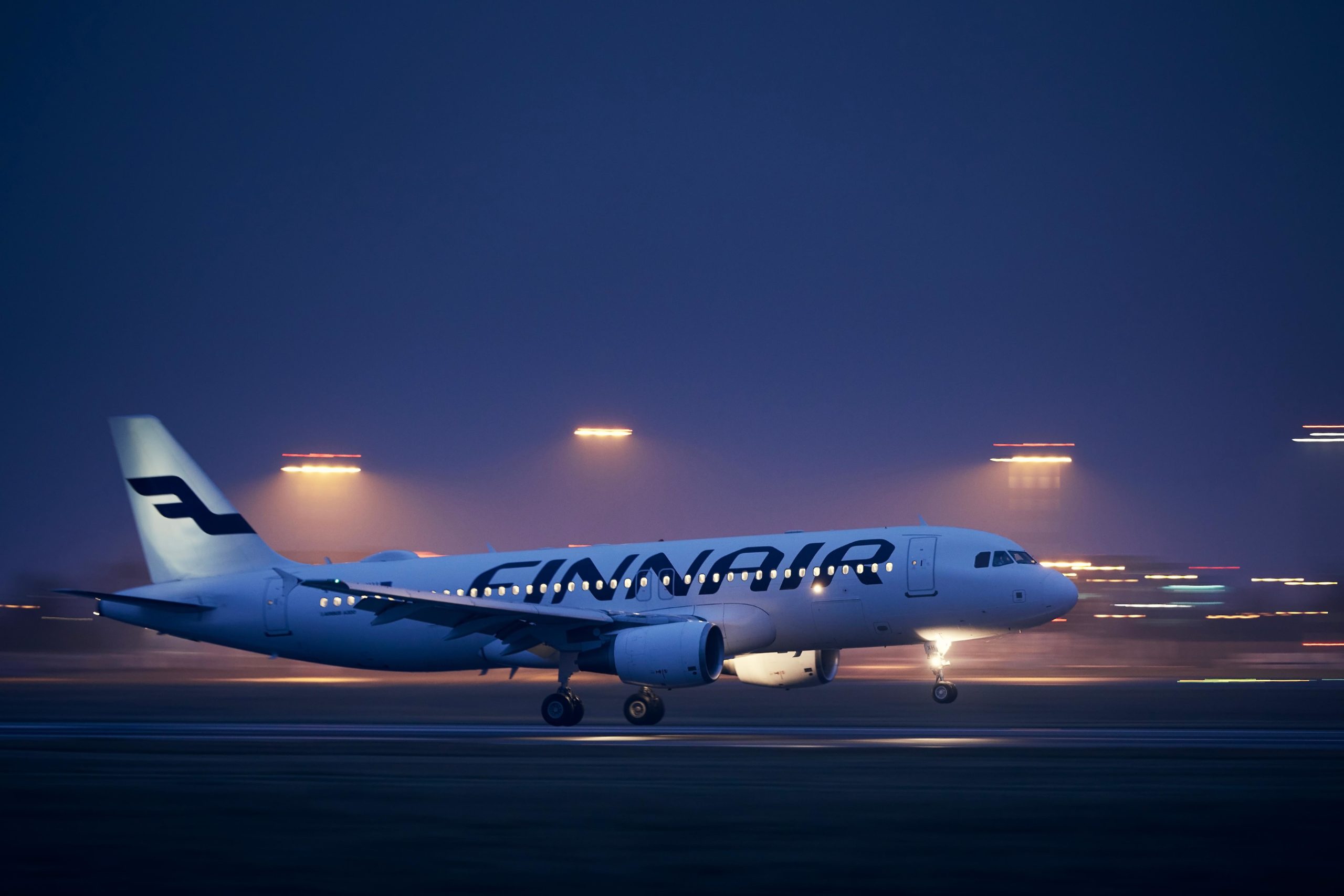 Finnair Airbus A320 laskeutumassa illalla lentokentälle. Taustalla olevat lentokentän valot ovat sumeita.