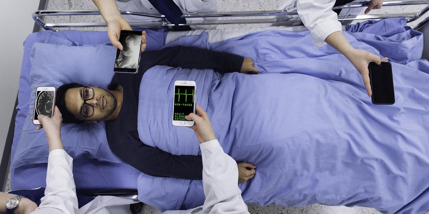 Man lying on a hospital bed while doctors perform diagnoses on their smart phones.
