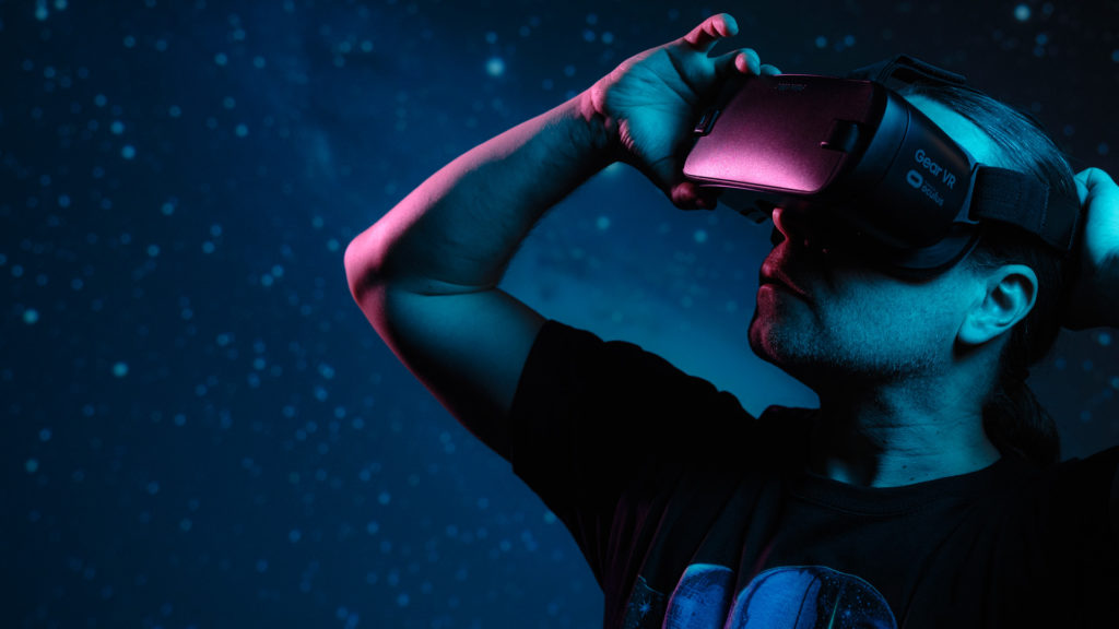 A person stands in front of the starry sky and looks to the left with VR glasses.