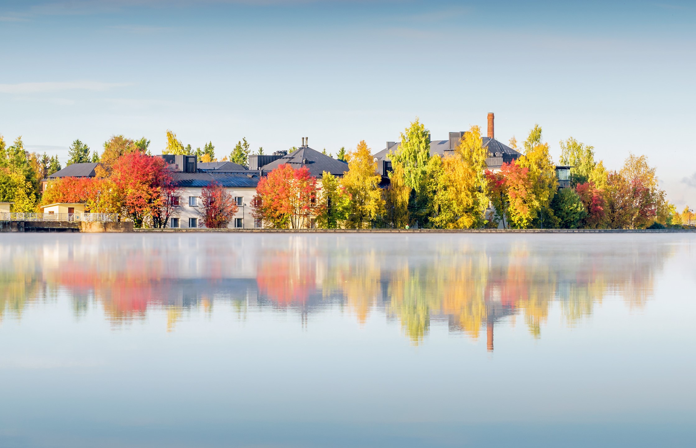 Colorful trees of Oulu's Lasaretinsaari reflected in the mirror-calm Oulujoki